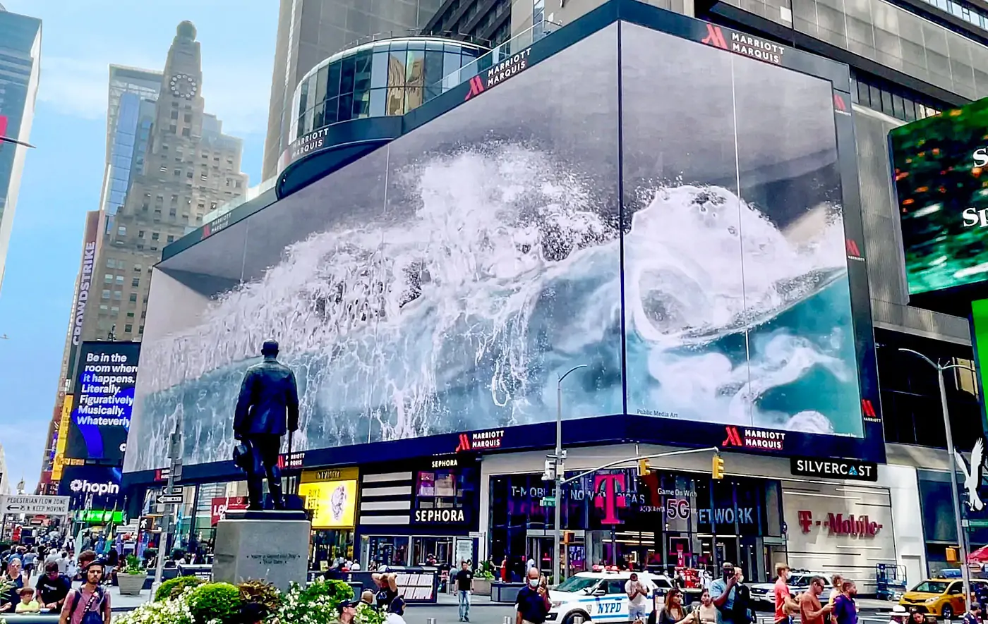 Corner wrap installations of 3D billboards LED Display Manufacturer in China EagerLED Busy Times Square scene with a huge wave advertisement on a curved billboard atop the Marriott Marquis a statue stands in the foreground as pedestrians pass by