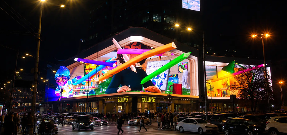 3D billboard2 LED Display Manufacturer in China EagerLED Nighttime city scene with a large building projection featuring oversized colorful glowing pencils and pedestrians nearby near a Gulliver store façade