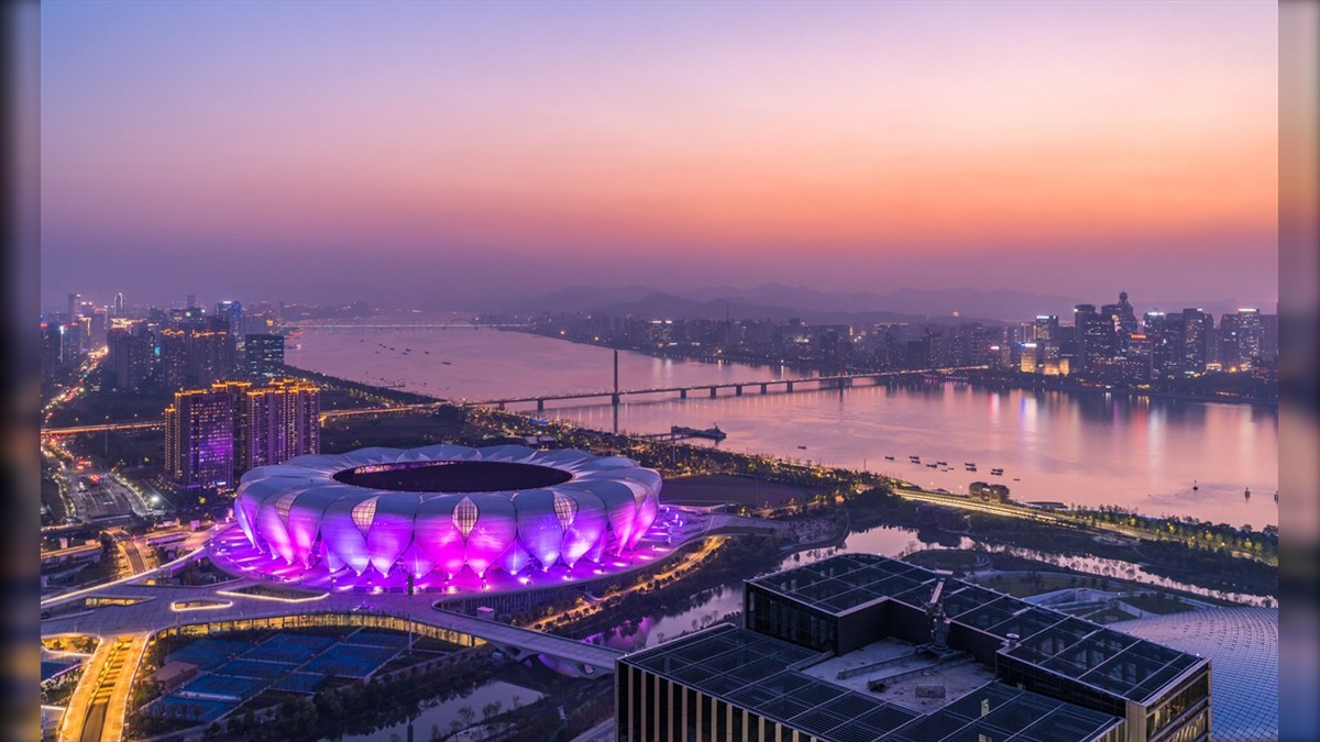 Hangzhou Asiatic Center Biggest LED Screen Project LED Display Manufacturer in China EagerLED Aerial view of a city at sunset with a large stadium illuminated in purple near a winding river and bridge