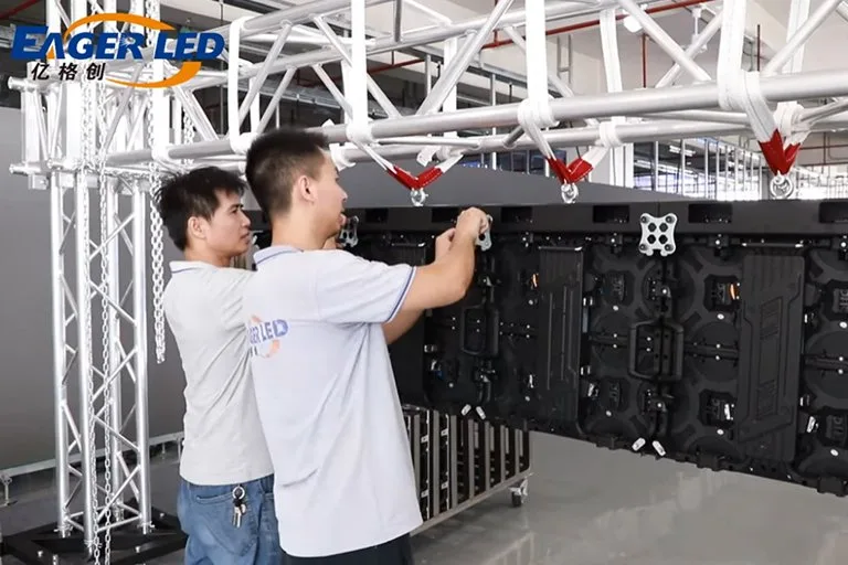 Two technicians installing rental LED cabinets on a hanging beam during an LED video wall installation
