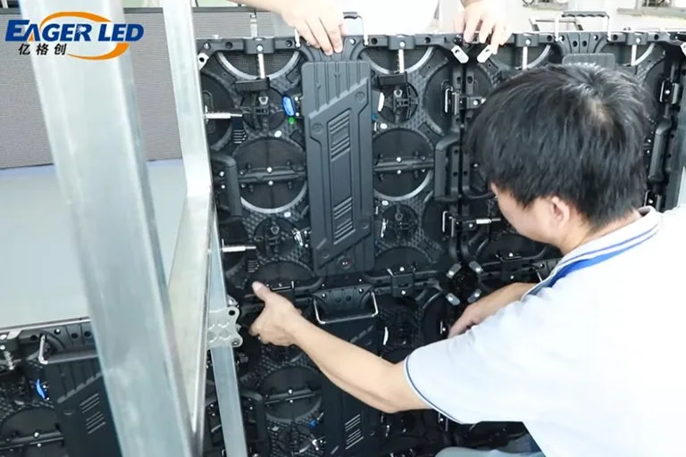 Technician ground-stacking rental LED cabinets beside a rear support bracket